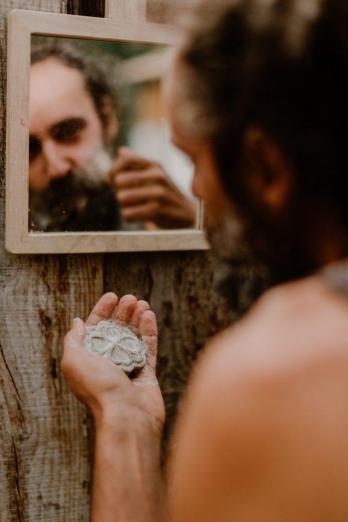 Un homme faisant face à un miroir, il tient un pain de savon à barbe dans sa main